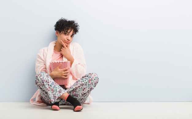 Young african american woman holding a popcorn bucket looking sideways with doubtful and skeptical expression.