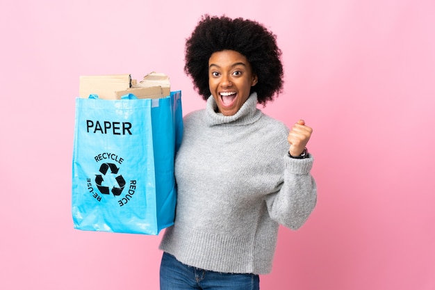 Young African American woman holding a recycle bag celebrating a victory in winner position