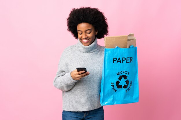 Young African American woman holding a recycle bag sending a message with the mobile