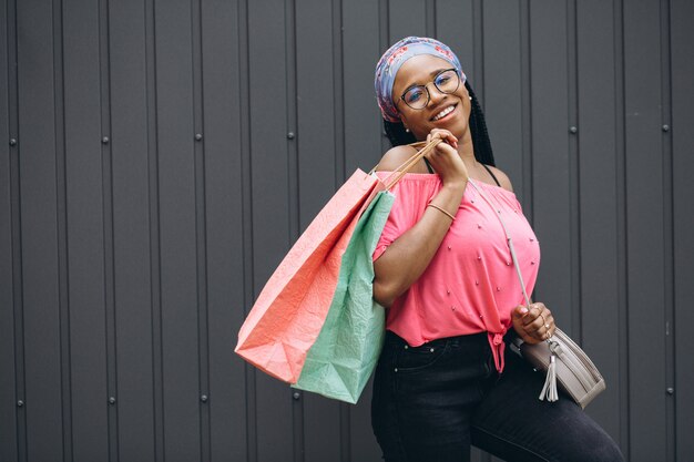 Young african american woman holding shopping bags at the gray wall