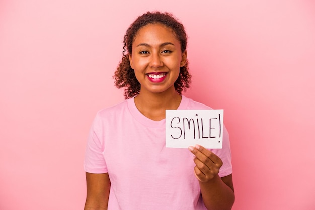 Photo young african american woman holding a smile placard isolated on pink background