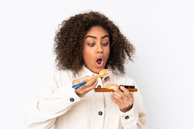 Young African American woman holding sushi on white wall