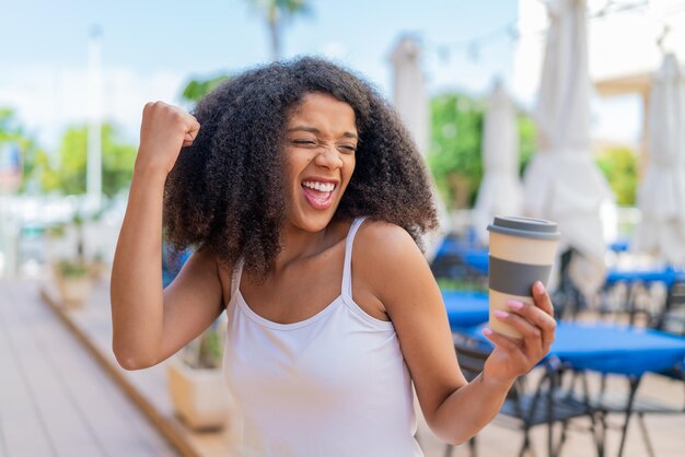 Photo young african american woman holding a take away coffee at outdoors celebrating a victory