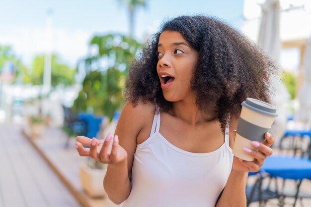 Young African American woman holding a take away coffee at outdoors with surprise facial expression