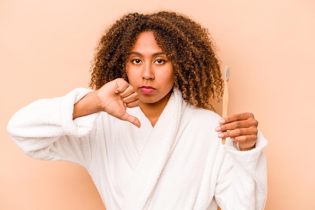 Young African American woman holding toothbrush isolated on beige background showing a dislike gesture thumbs down Disagreement concept