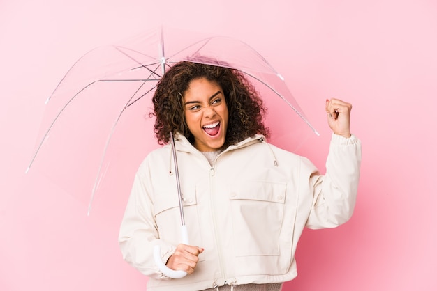 Young african american woman holding a umbrella raising fist after a victory, winner concept.