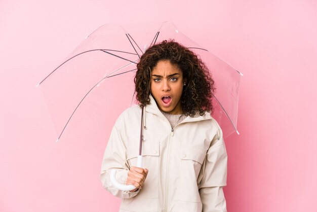 Young african american woman holding a umbrella screaming very angry and aggressive.