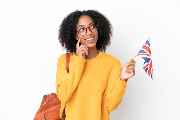 흰색 배경에 격리된 영국 국기를 들고 올려다보는 동안 아이디어를 생각하는 젊은 아프리카계 미국인 여성