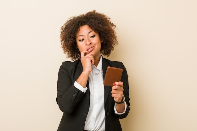 Young african american woman holding a wallet relaxed thinking about something looking at a copy space.