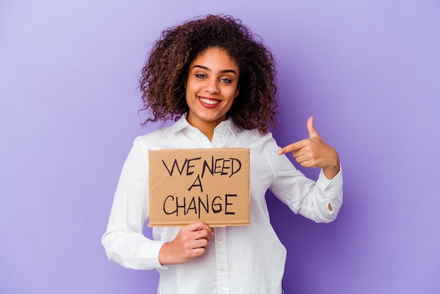 Young African American woman holding a We need a change placard isolated on purple person pointing by hand to a shirt copy space, proud and confident