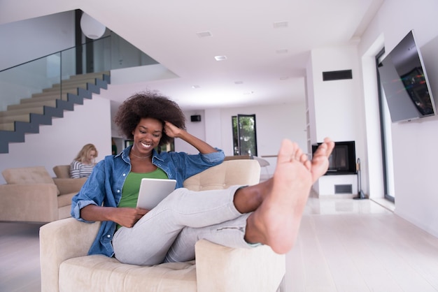 Young african american woman at home relaxing in her luxury lliving room reading a digital tablet PC surf internet and work