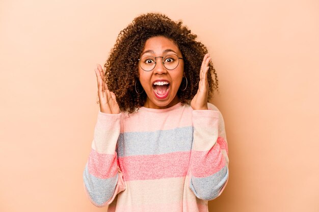 Young African American woman isolated on beige background celebrating a victory or success he is surprised and shocked