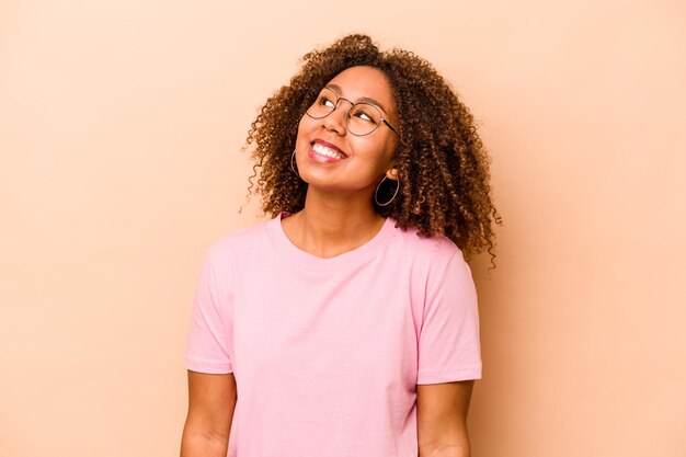 Young African American woman isolated on beige background relaxed and happy laughing neck stretched showing teeth