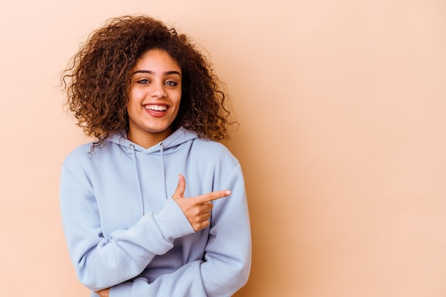 Young african american woman isolated on beige background smiling cheerfully pointing with forefinger away.