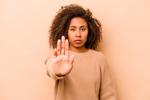 Young african american woman isolated on beige background\
standing with outstretched hand showing stop sign preventing\
you