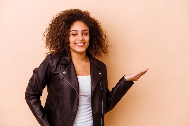 Young african american woman isolated on beige showing a copy space on a palm and holding another hand on waist.