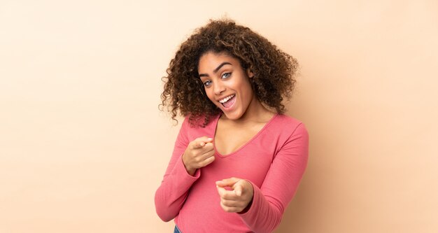 Young african american woman isolated on beige surprised and pointing front