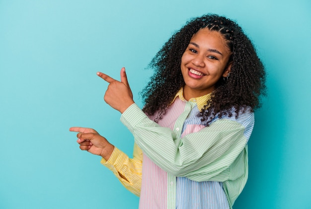 Young african american woman isolated on blue background pointing with forefingers to a copy space, expressing excitement and desire.