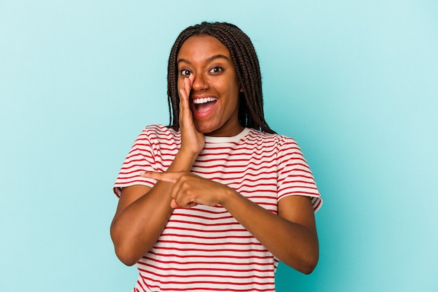 Young african american woman isolated on blue background  saying a gossip, pointing to side reporting something.