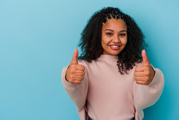 笑顔と親指を上げる青い背景に分離された若いアフリカ系アメリカ人女性