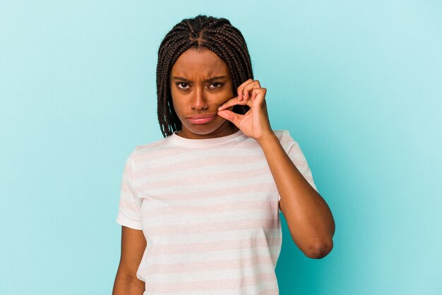 Молодая афро-американская женщина, изолированные на синем фоне с пальцами на губах, сохраняя в секрете.