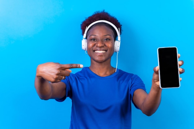 Young african american woman isolated on a blue background with mobile pointing gesture studio shoot