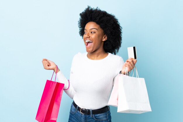 Young African American woman isolated on blue holding shopping bags and a credit card