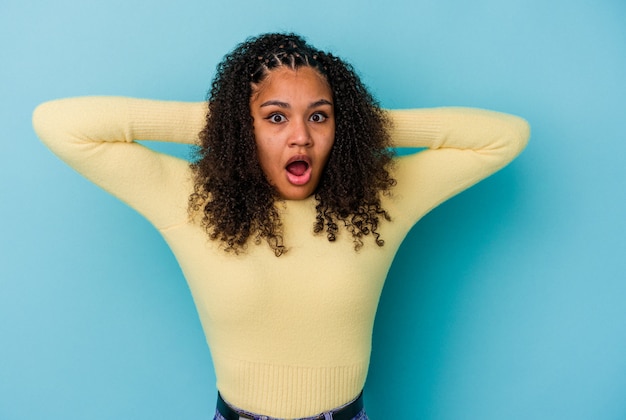 Young african american woman isolated on blue wall screaming, very excited, passionate, satisfied with something.