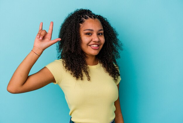 Young african american woman isolated on blue wall showing a horns gesture as a revolution concept.