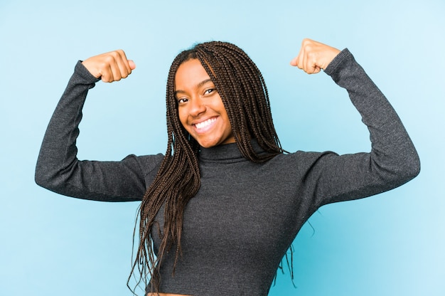 Young african american woman isolated on blue wall showing strength gesture with arms, symbol of feminine power