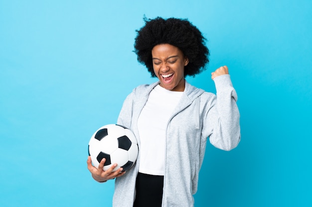 勝利を祝うサッカーボールと青に分離された若いアフリカ系アメリカ人女性