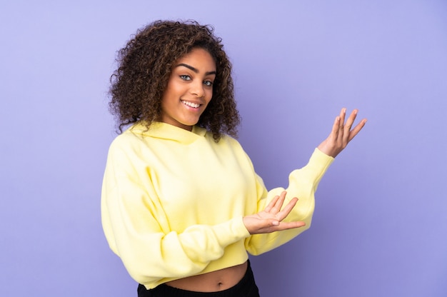 Young African American woman isolated on extending hands to the side for inviting to come