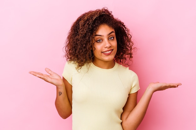 Young african american woman isolated on pink background confused and doubtful shrugging shoulders to hold a copy space.