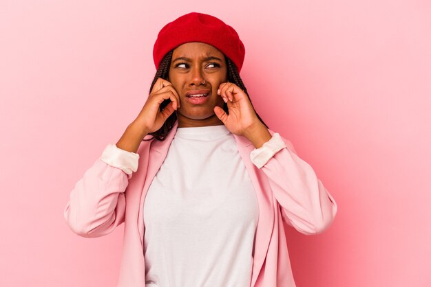 Young african american woman isolated on pink background  covering ears with fingers, stressed and desperate by a loudly ambient.