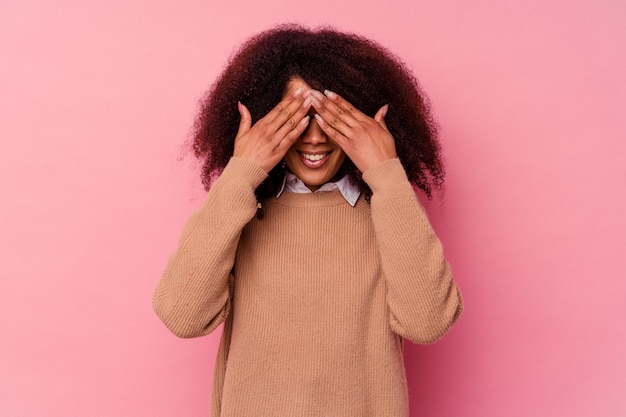 Young african american woman isolated on pink background covers eyes with hands, smiles broadly waiting for a surprise.