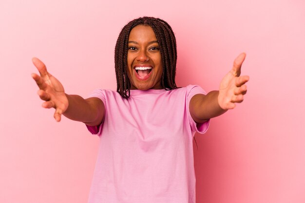 Молодая афро-американская женщина, изолированная на розовом фоне, чувствует себя уверенно, обнимая камеру.