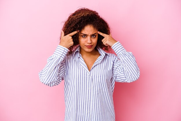 분홍색 배경에 고립 된 젊은 아프리카 계 미국인 여자는 머리를 가리키는 집게 손가락을 유지하는 작업에 초점을 맞춘.