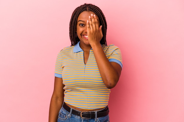 Молодая афро-американская женщина, изолированные на розовом фоне, весело закрывая половину лица ладонью.