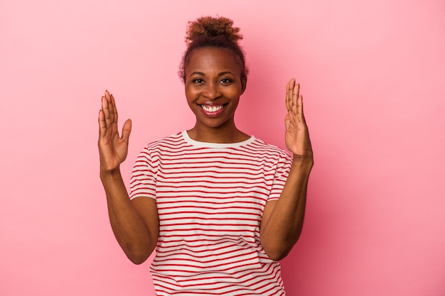 ピンクの背景に孤立した若いアフリカ系アメリカ人の女性は、人差し指で少し何かを保持し、笑顔で自信を持っています。