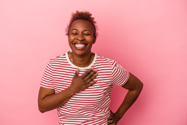 Giovane donna afroamericana isolata su fondo rosa che ride tenendo le mani sul cuore, concetto di felicità.