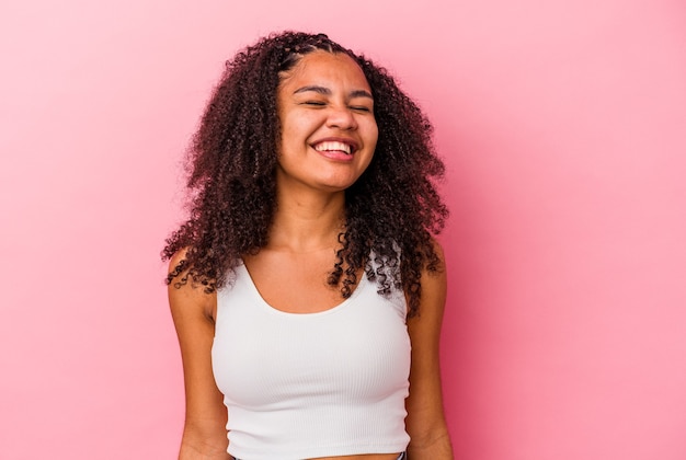 Young african american woman isolated on pink background laughs and closes eyes, feels relaxed and happy.