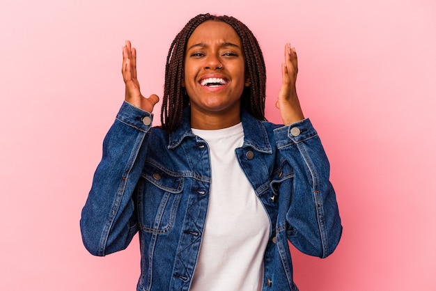 La giovane donna afroamericana isolata su fondo rosa ride ad alta voce tenendo la mano sul petto.