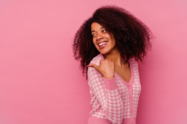 Young african american woman isolated on pink background points with thumb finger away, laughing and carefree.