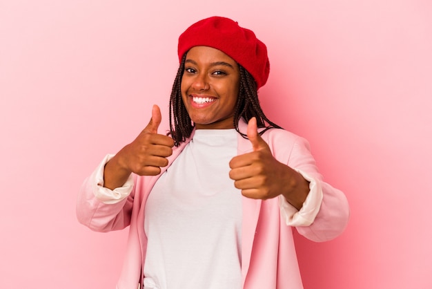 분홍색 배경에 격리된 젊은 아프리카계 미국인 여성은 두 엄지손가락을 위로 들고 웃고 자신감을 갖고 있습니다.