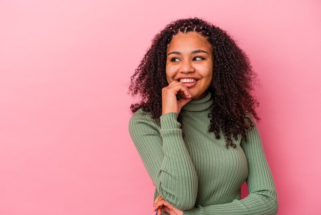 Young african american woman isolated on pink background relaxed thinking about something looking at a copy space.