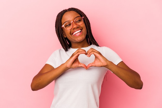 Молодая афро-американская женщина, изолированных на розовом фоне, улыбается и показывает форму сердца руками.