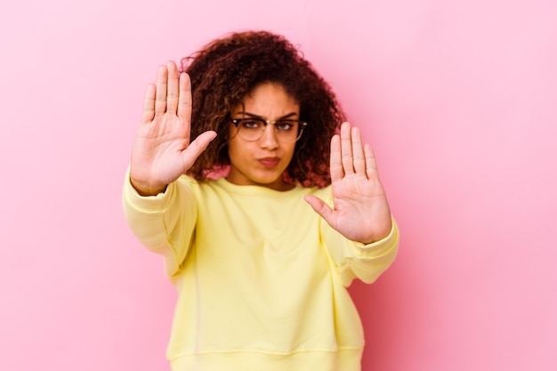 Young african american woman isolated on pink background standing with outstretched hand showing stop sign, preventing you.