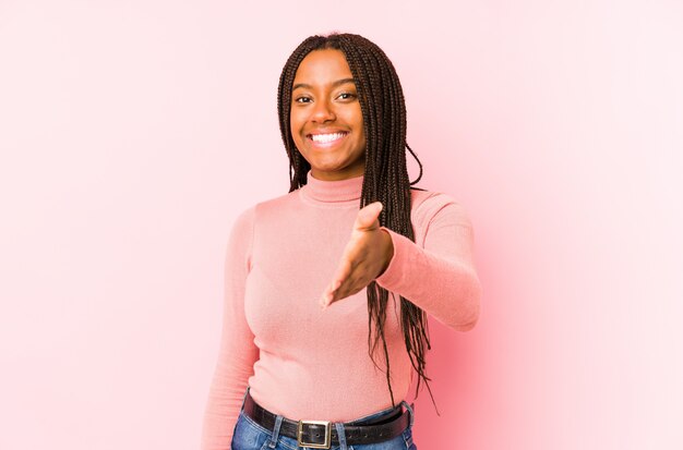 Young african american woman isolated on a pink background stretching hand at camera in greeting gesture.