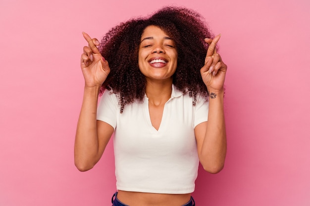 Young african american woman isolated on pink crossing fingers for having luck