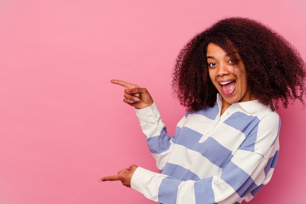 Young african american woman isolated on pink excited pointing with forefingers away.